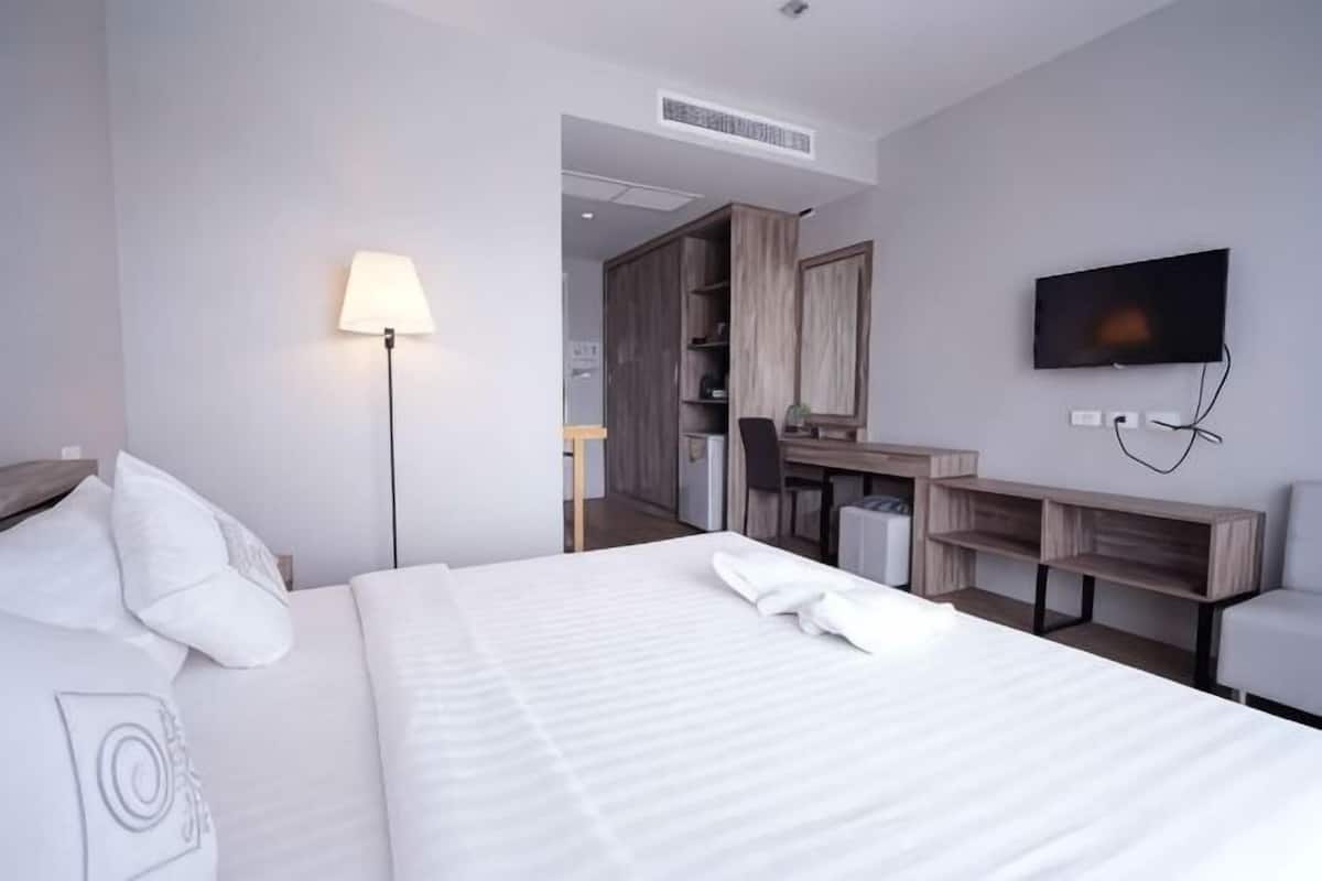 A hotel room with a bed, a desk, a TV, and a lamp.