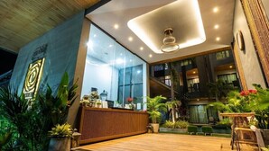 Un hall d’hôtel moderne avec un comptoir d’accueil, de grandes fenêtres et des plantes d’intérieur.