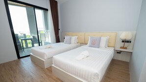 Une chambre d’hôtel avec deux lits, une grande porte-fenêtre coulissante donnant sur un espace extérieur et une table de chevet avec une lampe.