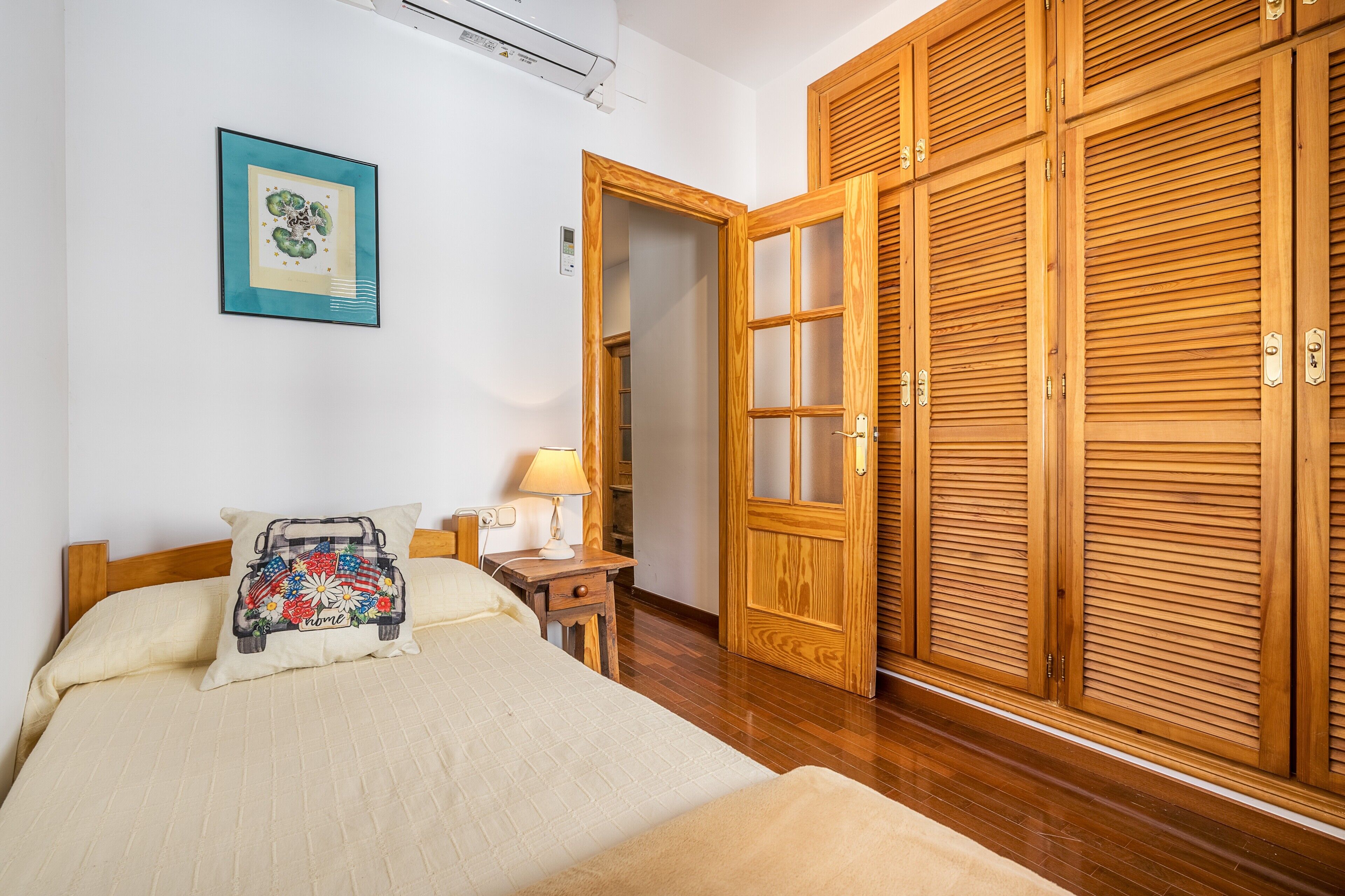 Un dormitorio con cama, mesita de noche, lámpara y un armario de madera.