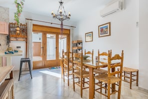 A dining area with wooden chairs and a glass table, a chandelier, and a view through a door.