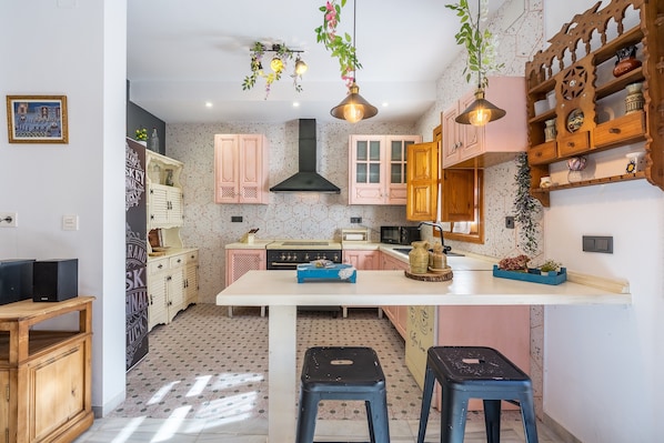 A kitchen with a central island, wooden cabinets, a black range hood, and hanging plants.