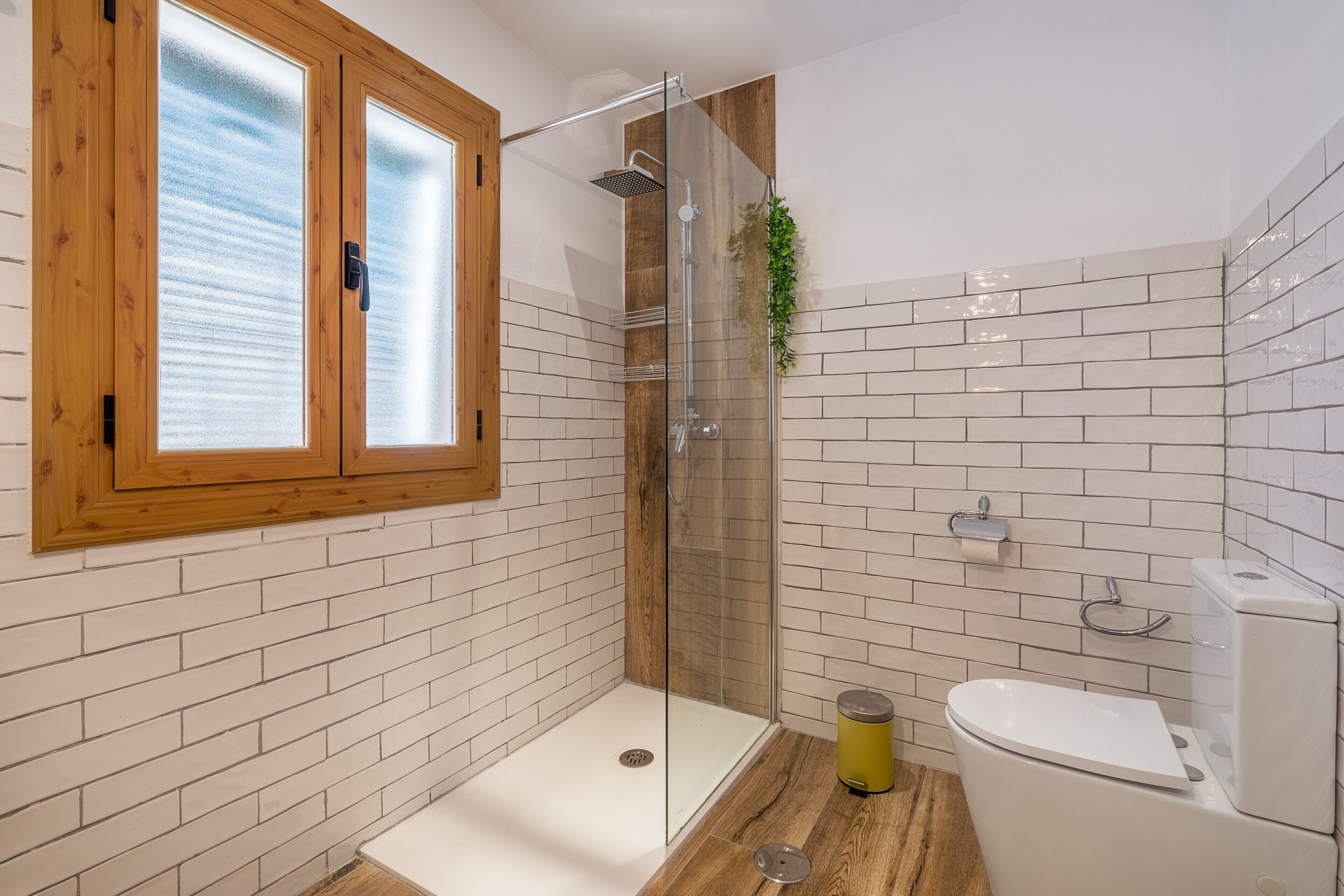 Ein Badezimmer mit einer Glasdusche, einer weißen Toilette und einem raumhohen Holzfenster.