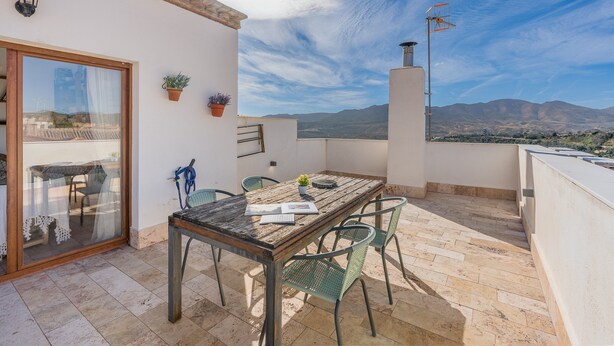A patio with a table and chairs, a potted plant, a wall-mounted light, and a view of distant mountains. - Vacation Home "El Valle Verde" with Mountain View, Private Terrace & Wi-Fi (Lecrin)