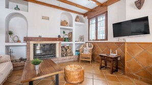 A living room with a fireplace, wooden beams, a TV, and a tiled floor. - Vacation Home "El Valle Verde" with Mountain View, Private Terrace & Wi-Fi (Lecrin)