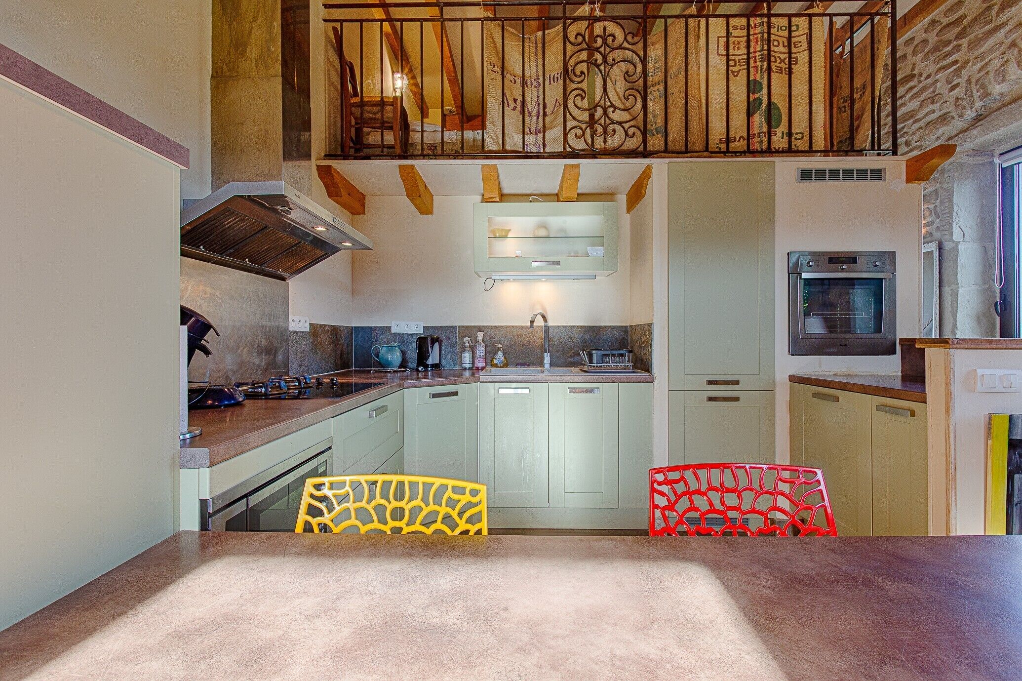 A kitchen with a central island, a built-in oven, and a dining area with two chairs.