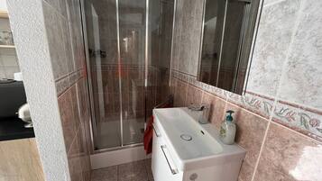 Un baño con ducha envuelta en vidrio, un lavamanos blanco con dispensador de jabón y un espejo sobre el lavamanos.