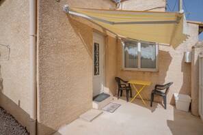 Une petite terrasse extérieure avec un auvent jaune à rayures, une porte blanche et deux chaises.