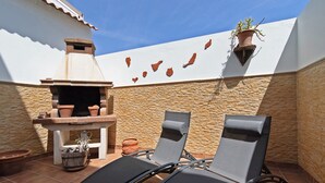 Une terrasse extérieure avec un mur en pierre, un barbecue, deux chaises longues et des plantes en pot.