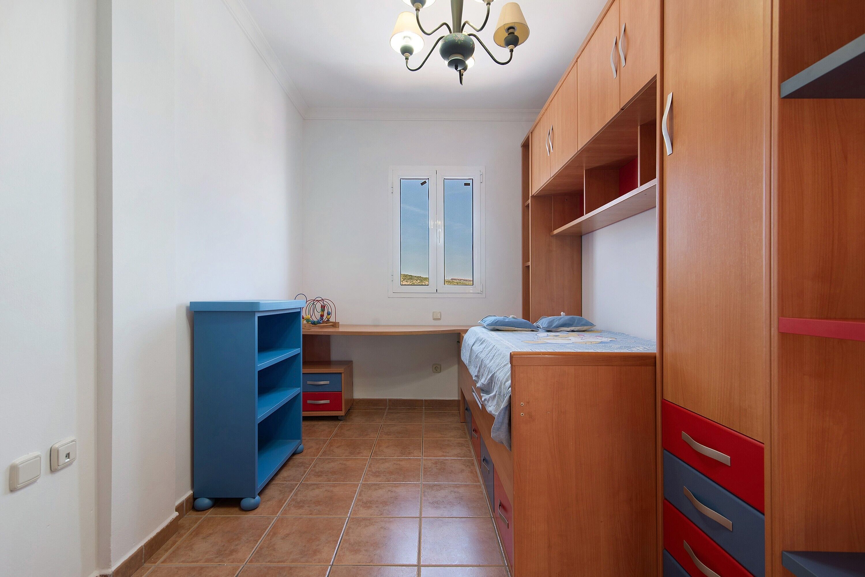 A bedroom with a bed, wardrobe, shelves, and a window.