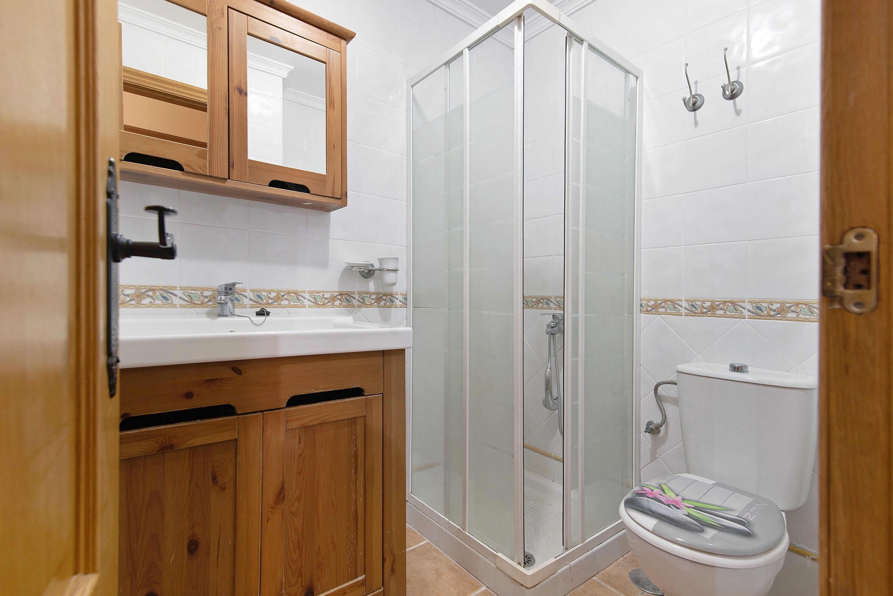 Un baño con un mueble de madera, un lavabo, un inodoro y una ducha con mampara de cristal.