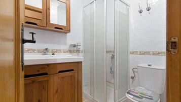 Un baño con un mueble de madera, un lavabo, un inodoro y una ducha con mampara de cristal.