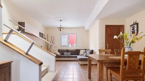 Un escalier mène à un espace de vie comprenant un canapé, une table à manger en bois, des chaises et un vase avec des fleurs.