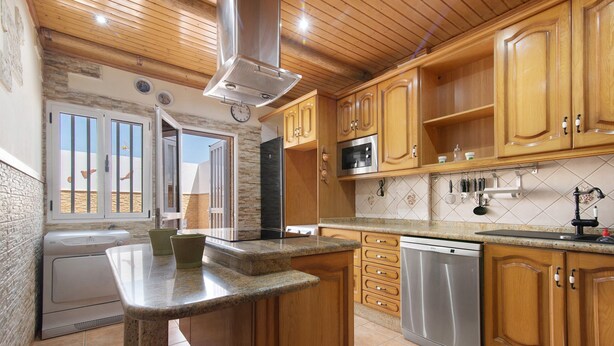 Une cuisine dotée de meubles en bois, de plans de travail en granit, d’appareils électroménagers en acier inoxydable et offrant une vue sur l’extérieur grâce à une porte ouverte.