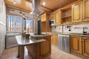 A kitchen with wooden cabinets, granite countertops, stainless steel appliances, and a view through an open door. - Holiday Villa 'Casa La Herradura' with Sea View, Private Terrace & Wi-Fi (Telde)