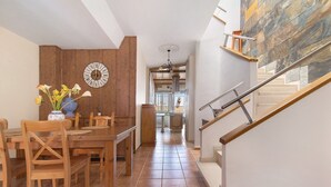 Un coin repas avec des meubles en bois, une horloge au mur et un escalier menant à l’étage supérieur.