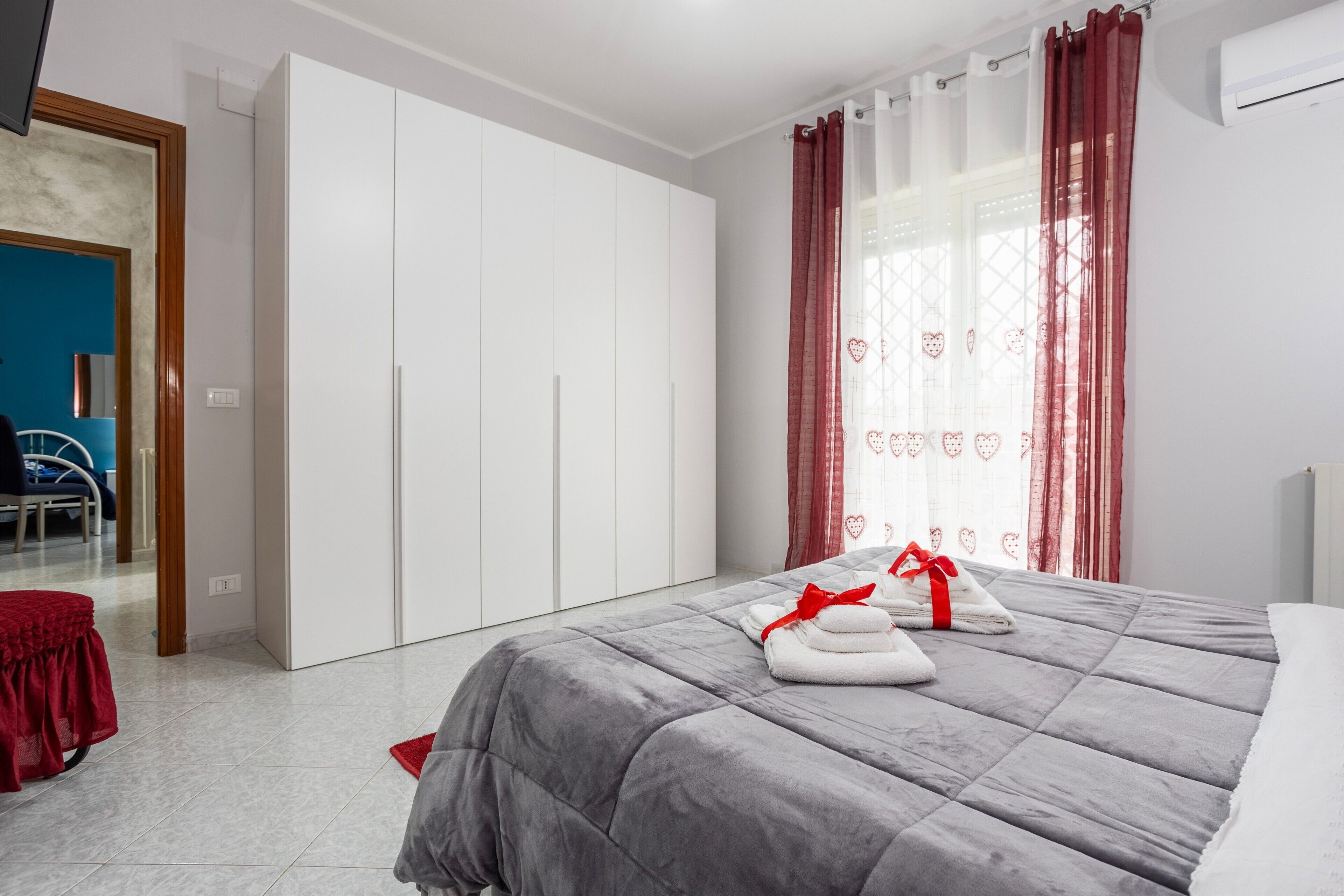 Een slaapkamer met een bed, een kledingkast, een rode stoel en uitzicht op een blauwe kamer.