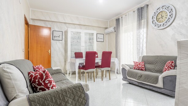 Ein Wohnzimmer mit einer Couch, einem Esstisch mit Stühlen und einer Uhr an der Wand.