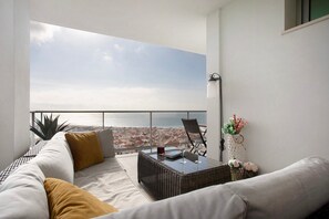 A balcony with a view of the sea, a wicker table with glasses, a sofa, and a wall-mounted lamp. - Nazaré Sea View Dream Apartment with Ocean View (Nazaré)