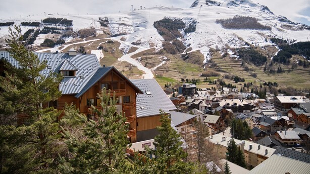 A mountain lodge with a wooden exterior, multiple balconies, and a view of a snow-covered mountain range. - Studio 'Les 2 Alpes' with Mountain View and Balcony (Les Deux Alpes)
