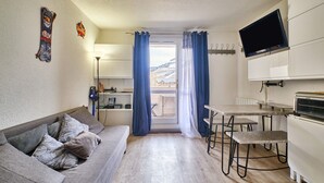 A compact living space with a sofa, a dining table, a TV, and a view through a window. - Studio 'Les 2 Alpes' with Mountain View and Balcony (Les Deux Alpes)
