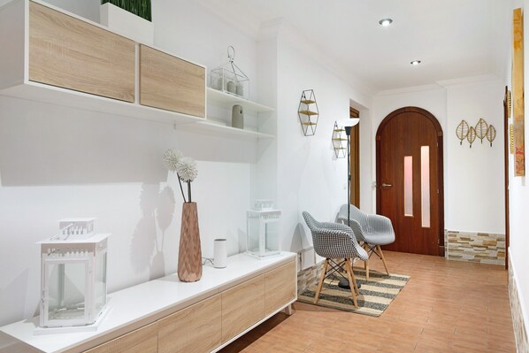 A modern living room with a white console table, wooden shelves, a patterned chair, and a wooden door.