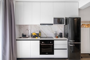 A modern kitchen with white cabinets, a black refrigerator, a built-in oven, and a microwave.