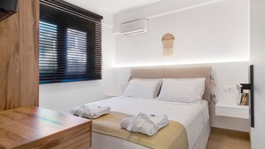 A hotel room with a bed, bedside table, wall-mounted air conditioner, and a small shelf with books. - Apartment 'Mella Roa Emer' with Sea View, Wi-Fi and Air Conditioning (???????)