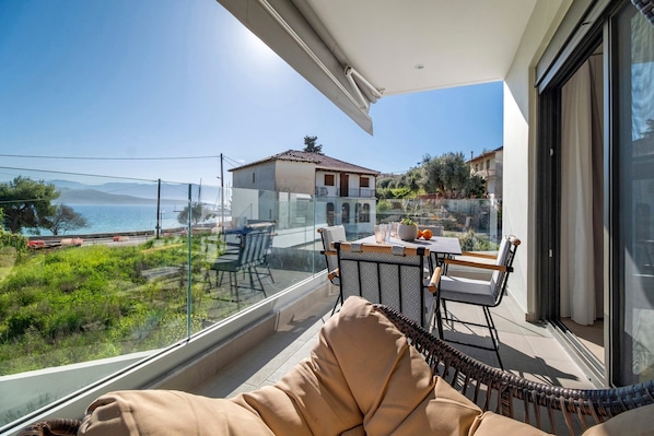 A balcony with a view of the sea, a dining table, and a wicker chair.