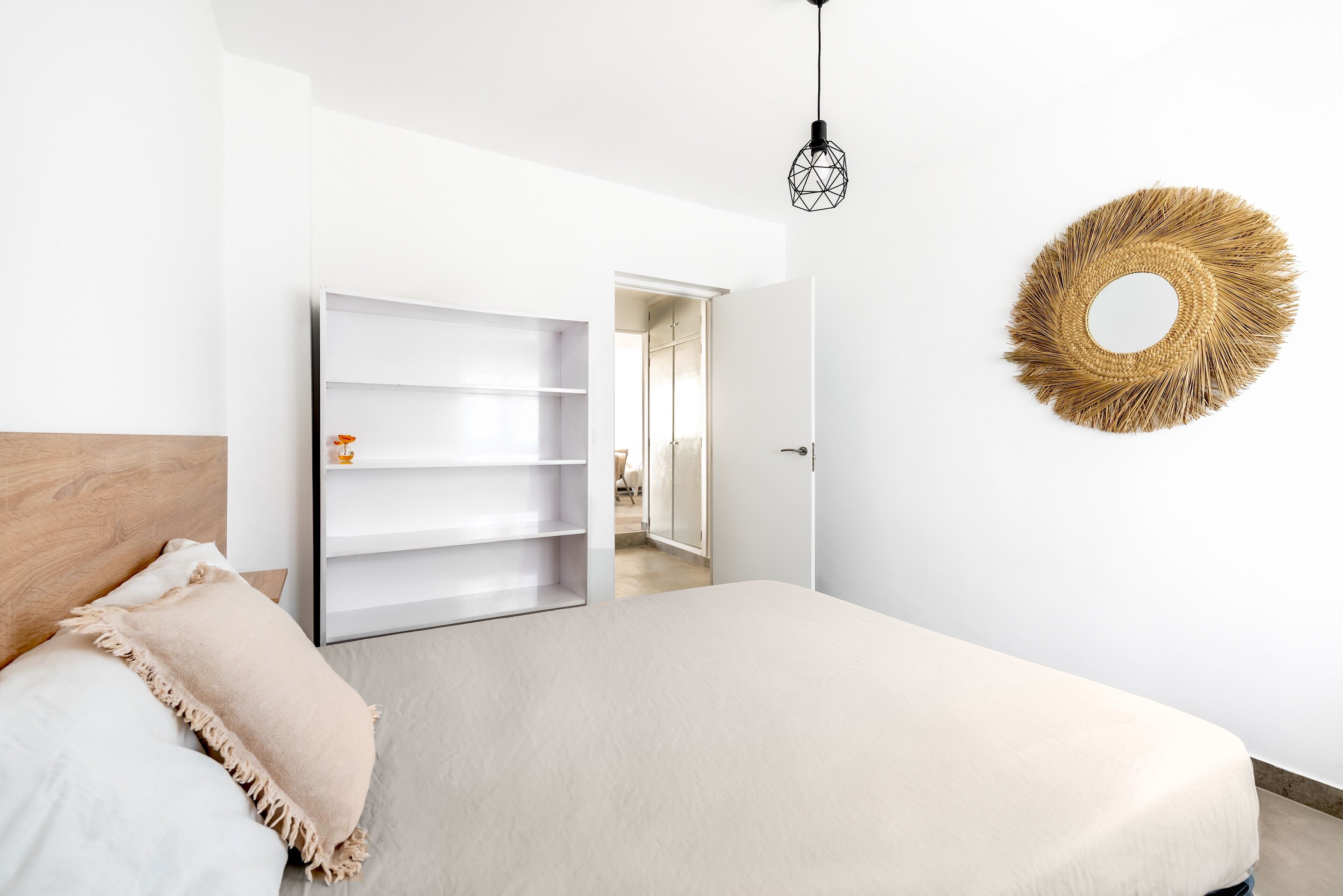 Une chambre à coucher comprenant un lit, une armoire, un miroir et un luminaire suspendu.