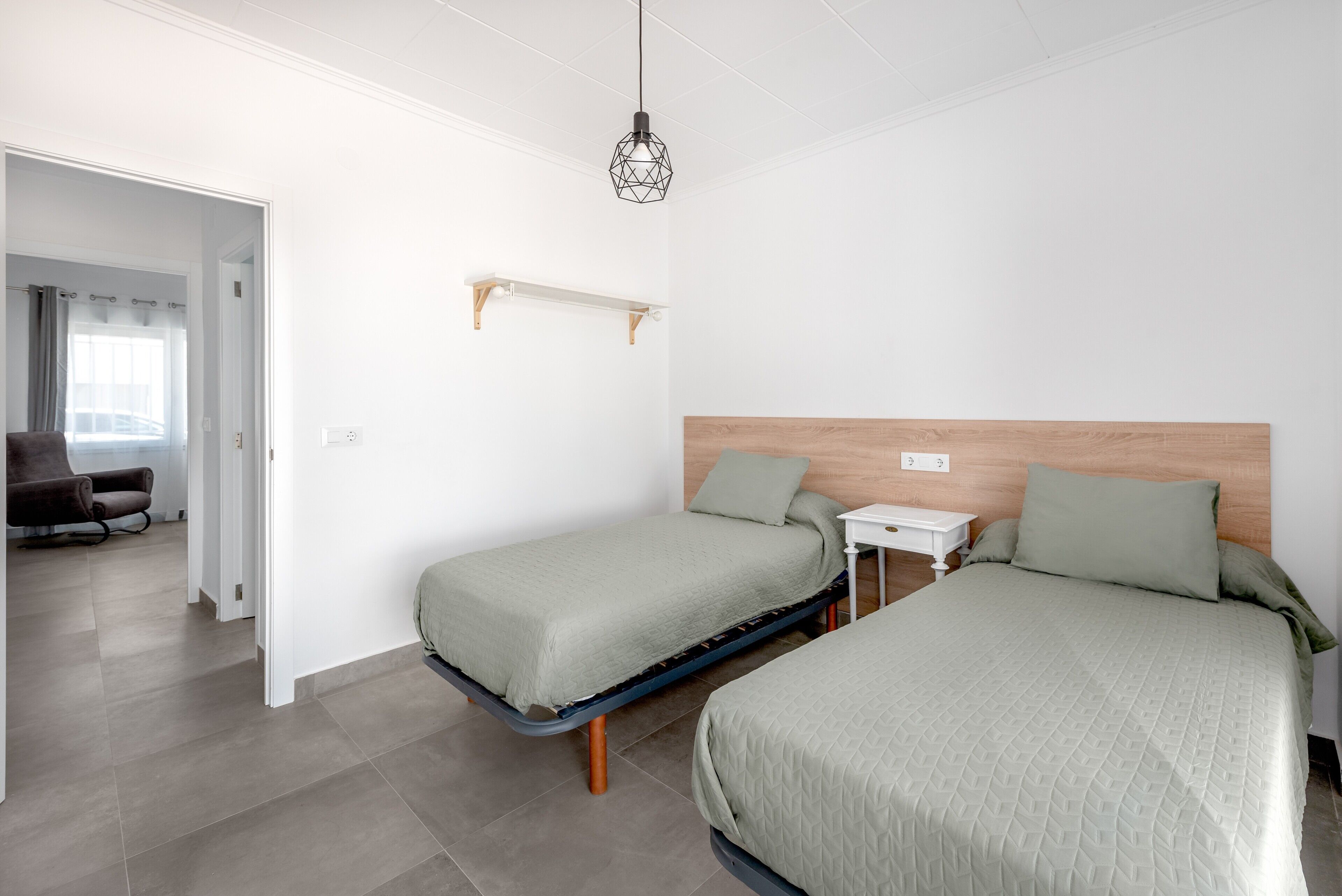 Una habitación con dos camas, una mesita de noche pequeña, una lámpara colgante y una silla.