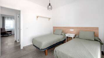 Una habitación con dos camas, una mesita de noche pequeña, una lámpara colgante y una silla.