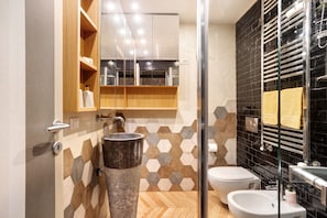Een moderne badkamer met een houten wastafelmeubel, een grote spiegel, een glazen douchecabine en een wand betegeld met zwarte tegels.