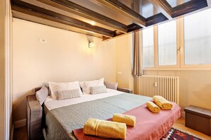 A neatly made bed with pillows, a bedside table, a radiator, and a window with blinds. - Apartment 'Dezza Loft' with Private Terrace, Wi-Fi and Air Conditioning (Milano)
