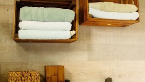 Un baño con estantes de madera que sostienen toallas dobladas, una cesta tejida y una escalera de madera.