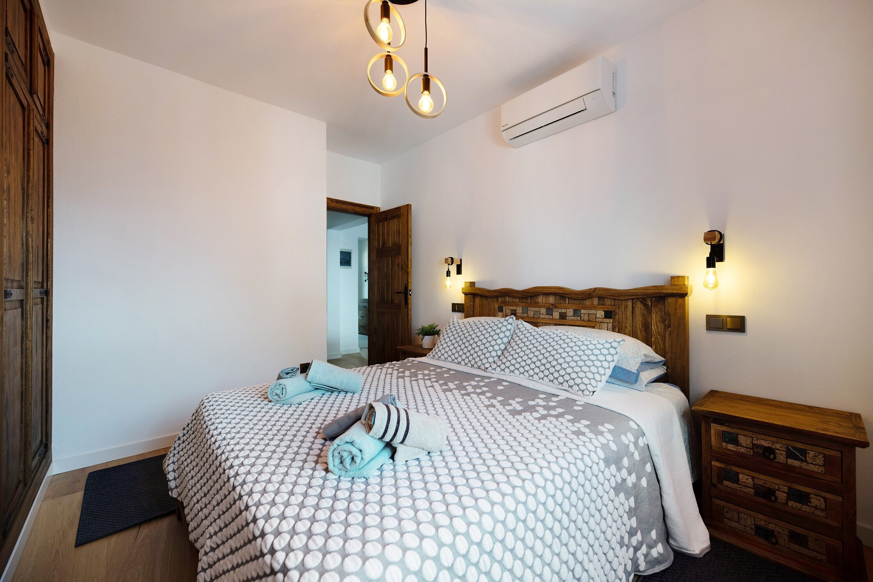 Une chambre à coucher comprenant un lit, des tables de chevet, une tête de lit en bois et un luminaire fixé au mur.