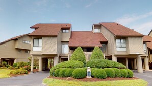 A modern multi-story residential building with a symmetrical design, featuring a central landscaped area with neatly trimmed bushes and a small fountain.