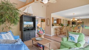 A spacious living room with a television, a globe, and a sailboat decoration. There is a dining area with a table and chairs.