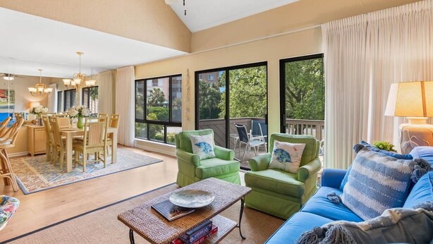 A spacious living room with a dining area, large windows with a view, and a ceiling fan.