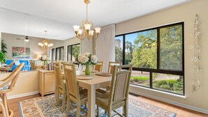 A dining area with a large table, wicker chairs, and a chandelier.