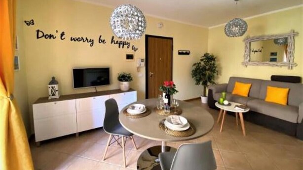 A cozy living room with a dining area, a sofa, a TV, and a motivational wall quote. - White Heron Residence (Ronchi dei Legionari)