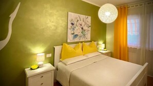 A bedroom with a bed, two bedside tables, a wall painting, a hanging light fixture, and a window with curtains. - White Heron Residence (Ronchi dei Legionari)