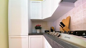 A kitchen with white cabinets, a granite countertop, a stove, and a wooden cutting board. - White Heron Residence (Ronchi dei Legionari)