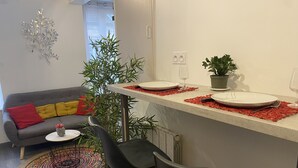 Uma cozinha moderna com área de jantar, apresentando um sofá cinza, cadeiras pretas, uma mesa pequena com um vaso e uma planta em vaso.