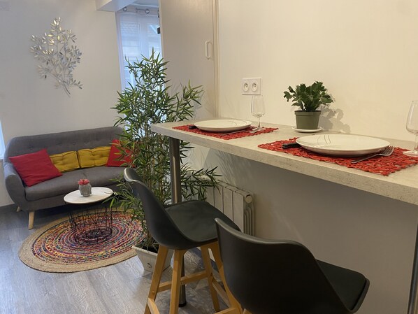 Una cocina moderna con comedor, que incluye un sofá gris, sillas negras, una mesita con un florero y una planta en maceta.
