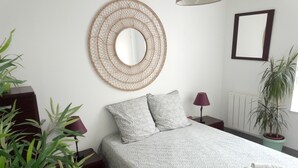 Quarto bem arrumado com uma cama, duas almofadas, abajur, espelho fixado na parede e planta em vaso.