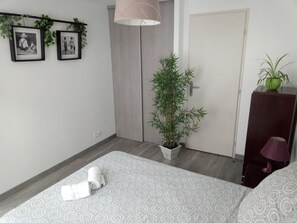 Relax in a serene bedroom with a neatly made bed, a potted bamboo plant, and a wall-mounted shelf.