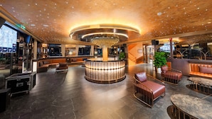 Un hall d’entrée moderne doté d’un bar circulaire central, de coins salon et d’un lustre.