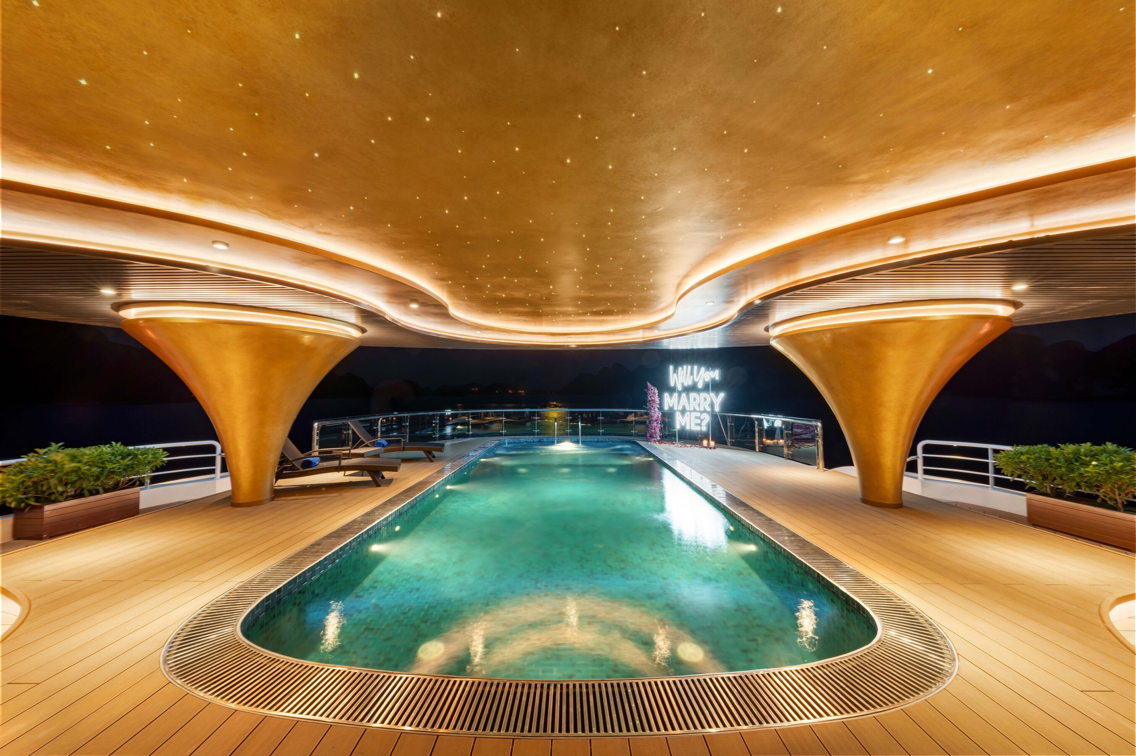 A pool area with a central pool, surrounded by wooden decking and a curved ceiling with embedded lights.