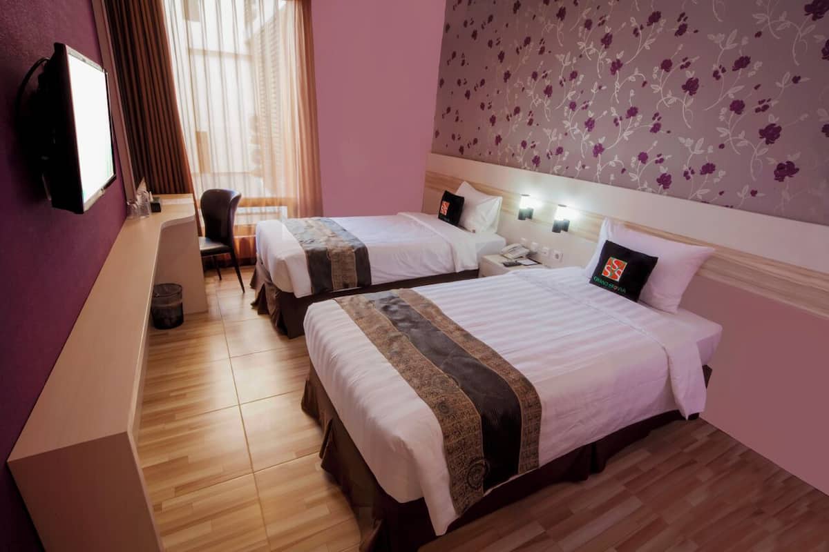 Ett hotellrum med två sängar, ett skrivbord, en stol och en tv.